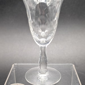 May include: A clear glass stemmed shot glass with a textured, rippled design. The glass has a round base and a tall, slender stem.