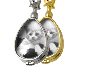 May include: Two teardrop-shaped cremation pendants with a photo of a cat inside. One pendant is silver and the other is gold.