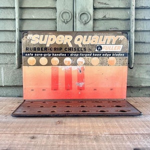 May include: Vintage metal sign for Fuller Rubber-Grip Chisels. The sign is orange and black with the text "SUPER QUALITY" and "RUBBER-GRIP CHISELS by FULLER". The sign has a display rack with holes for holding chisels.