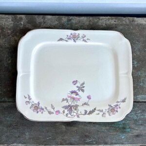 May include: A white rectangular serving platter with a gold rim and a floral design in shades of pink and purple.
