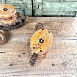 May include: Two vintage wooden pulley blocks with metal hardware. The larger block has the text "The Graphite Bronze" printed on it.
