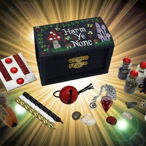 May include: A black wooden box with a painted design of mushrooms and the words "Harm Ye None". The box is open and contains various items, including a red bell, a feather, candles, a red crystal, and small bottles.