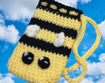 May include: A crocheted yellow and black bee-themed phone case with a white strap. The case has two black eyes and white wings.
