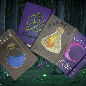 May include: Five purple and gray journals with different designs. The journals have titles that include "Potions", "Miracles", "Blessed", "Mists", and "Moon Beam". Each journal has a different design, including a potion bottle, a crescent moon, a triquetra, and a bottle with a feather inside.