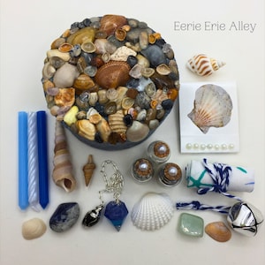 May include: A round box covered in seashells, surrounded by various sea-themed items, including candles, shells, a pendulum, and a small bell. The text "Eerie Erie Alley" is written in the top right corner of the image.