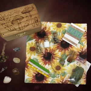 Pode incluir: Uma caixa de madeira com um desenho de cogumelo, um pequeno bloco de notas listrado branco e verde, duas pequenas garrafas de vidro com rolhas de cortiça, um colar de ouro com um pingente de cristal transparente, um pequeno saco de ervas secas rotulado como "Menta", e uma variedade de pequenos objetos, incluindo conchas, pedras e uma pequena caixa de madeira.