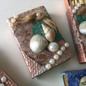 May include: A small, decorative box with a map-like design and a copper-colored finish. The box is adorned with white pearls, seashells, and a green and blue background.