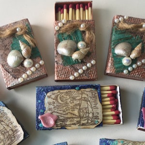 May include: Six matchboxes decorated with various nautical themes.  The matchboxes feature seashells, pearls, and a ship on a map.  The matchboxes are a great way to add a touch of nautical charm to your home.
