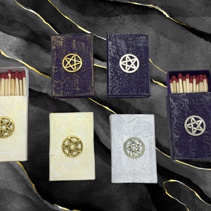May include: Six matchboxes with a pentagram design. The matchboxes are in various colors, including white, gold, silver, and purple. Each matchbox has a different pentagram design.