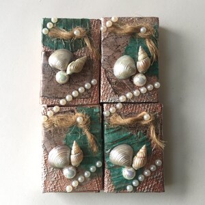 May include: Four small square boxes with a green and brown background. Each box has a different seashell design with pearls and twine.