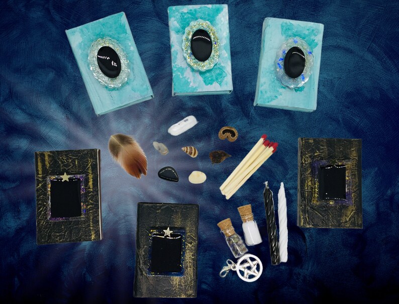 May include: An assortment of mystical items arranged on a dark blue background. The items include three teal-colored books with oval embellishments, three black books with star accents, a feather, stones, shells, matches, candles, and small bottles.