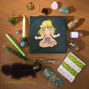 Pode incluir: Uma pintura em tela verde com uma mulher de cabelo amarelo meditando com uma espiral na barriga. A pintura é cercada por vários objetos, incluindo velas, cristais, uma pena, um sino pequeno e um pedaço de tecido enrolado. O texto "Eerie Erie Alley" está escrito na parte inferior da imagem.