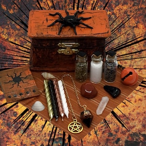 May include: A wooden box with a black spider painted on the lid, surrounded by various items including candles, crystals, herbs, and a pendulum. The box is decorated with an orange and black paint scheme, and the items are arranged on a brown fabric surface.