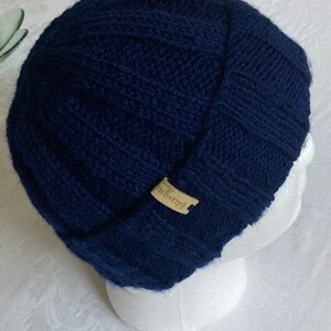 K&ouml;nnte beinhalten: Eine dunkelblaue Strickm&uuml;tze mit einem kleinen braunen Etikett mit der Aufschrift "Hand-Knit".
