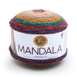 May include: A round cake of Lion Brand Mandala yarn featuring a gradient of colors including purple, teal, gold, and beige. The white paper label displays the Lion Brand Yarns logo, the word MANDALA in large letters, and LIONBRAND.COM text.