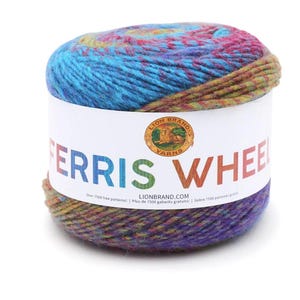 May include: A ball of variegated yarn featuring a blend of blue, purple, green, and pink tones. A white paper label wraps around the center, displaying the Lion Brand Yarns logo and the text FERRIS WHEEL in multicolored, bold, capital letters.