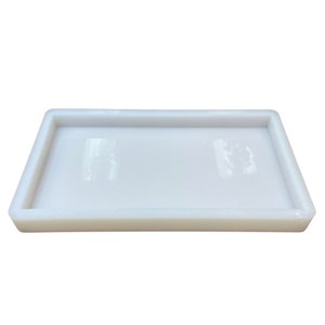Peut inclure: Un plateau rectangulaire blanc avec un bord surélevé. Le plateau est fait d'un matériau lisse et brillant.