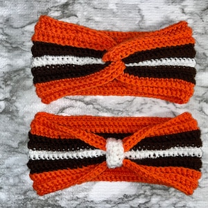 May include: Two crocheted headbands in orange, brown, and white stripes. The headband on top has a knotted design, while the headband on the bottom has a white bow.