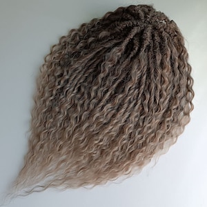 May include: A bundle of pre-twisted, ombre hair extensions. The hair transitions from dark brown at the roots to light blonde at the ends. The texture is curly and the hair is arranged in a teardrop shape.