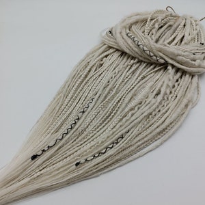 May include: A bundle of white synthetic dreadlocks with black stitching. The dreadlocks are long and thick, and they are arranged in a loose, flowing style.