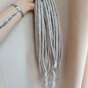 May include: A set of grey and white synthetic dreadlocks. The dreadlocks are long and have a wavy texture.