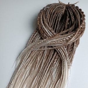 May include: A bundle of synthetic dreadlocks in shades of brown and blonde. The dreadlocks are ombre, with the brown color fading to blonde at the ends.