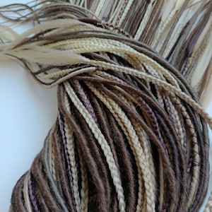 May include: A bundle of brown, blonde, and light brown synthetic dreadlocks. The dreadlocks are arranged in a circular pattern.