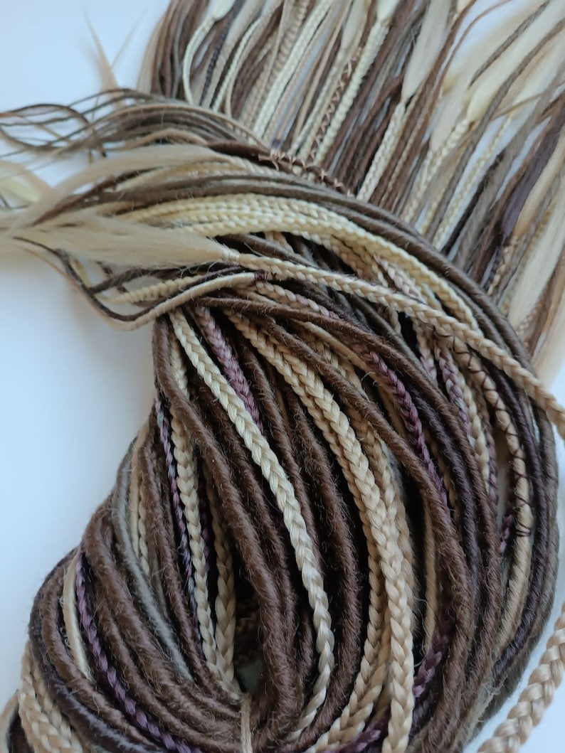 May include: A bundle of brown, blonde, and light brown synthetic dreadlocks. The dreadlocks are arranged in a circular pattern.