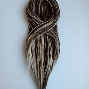 May include: A bundle of brown, blonde, and white synthetic hair extensions. The extensions are braided and tied together at the top.