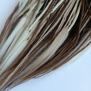May include: A set of brown, beige and blonde synthetic dreadlocks. The dreadlocks are braided and have a variety of textures.