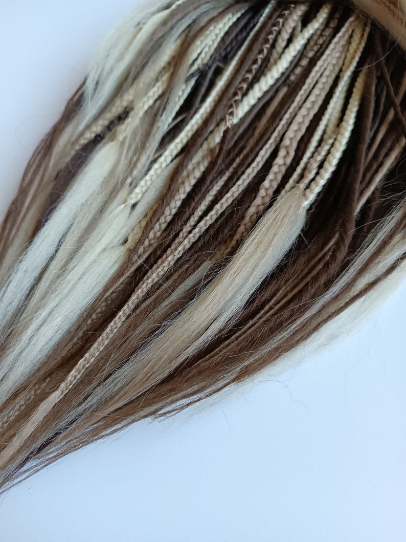 May include: A set of brown, beige and blonde synthetic dreadlocks. The dreadlocks are braided and have a variety of textures.