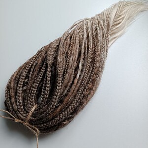 May include: A bundle of brown and blonde ombre synthetic dreadlocks. The dreadlocks are tied together with a brown string.