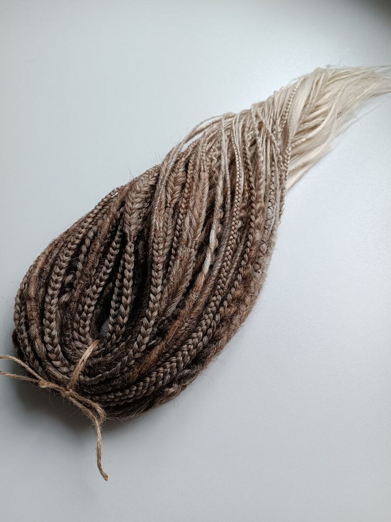 May include: A bundle of brown and blonde ombre synthetic dreadlocks. The dreadlocks are tied together with a brown string.