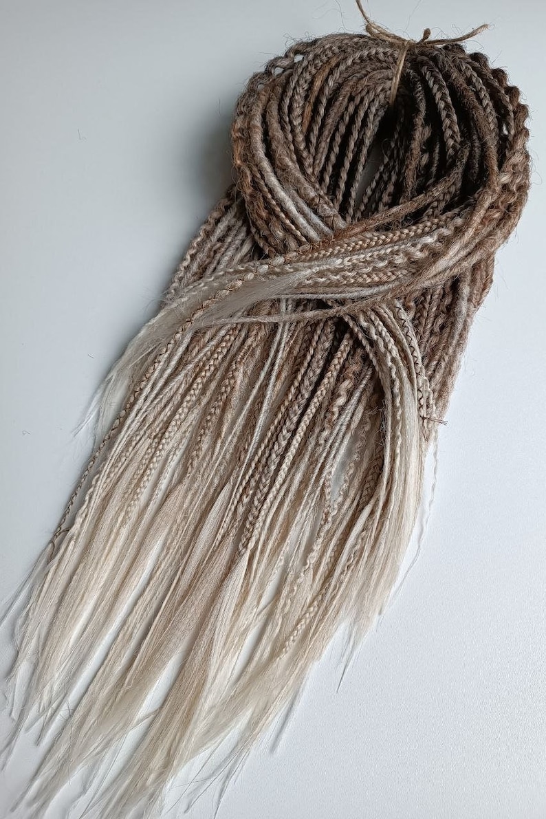 May include: A bundle of synthetic dreadlocks in shades of brown and blonde. The dreadlocks are ombre, with the brown color fading to blonde at the ends.