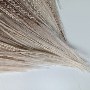 May include: A bundle of blonde and light brown synthetic hair extensions. The hair is long and straight, with a variety of shades of blonde and brown.