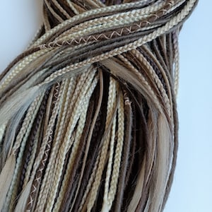 May include: A bundle of brown, beige, and blonde synthetic hair extensions. The extensions are braided and have a variety of textures.