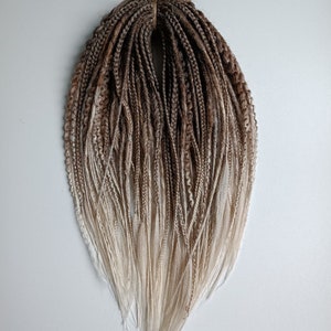May include: A set of brown and blonde ombre synthetic dreadlocks. The dreadlocks are tied together with a brown string.