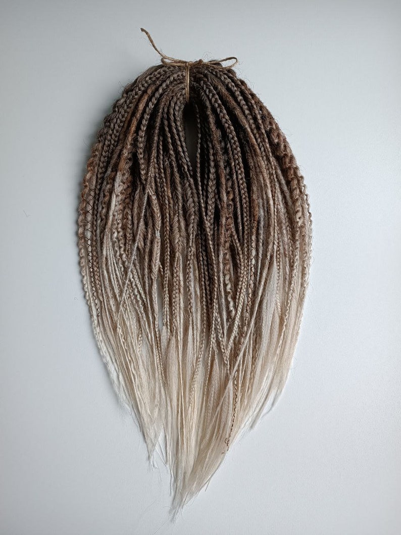 May include: A set of brown and blonde ombre synthetic dreadlocks. The dreadlocks are tied together with a brown string.