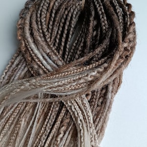 May include: A bundle of brown and blonde synthetic hair extensions. The hair is braided and tied together with a string.