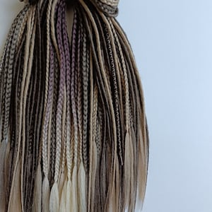 May include: A set of brown, beige and light blonde synthetic dreadlocks. The dreadlocks are 45 cm long and are tied together at the top.