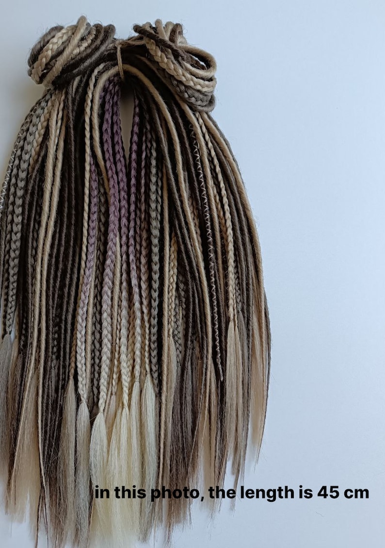 May include: A set of brown, beige and light blonde synthetic dreadlocks. The dreadlocks are 45 cm long and are tied together at the top.