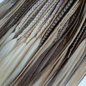 May include: A collection of synthetic dreadlocks in shades of brown, beige, and blonde. The dreadlocks are arranged in a fan shape, with the tips of the dreadlocks pointing towards the bottom of the image.