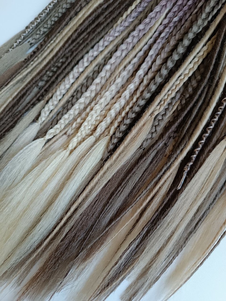 May include: A collection of synthetic dreadlocks in shades of brown, beige, and blonde. The dreadlocks are arranged in a fan shape, with the tips of the dreadlocks pointing towards the bottom of the image.