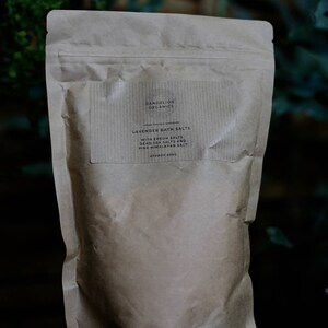 May include: A brown paper bag of Dandelion Organics Lavender Bath Salts. The label reads "With Epsom Salts, Dead Sea Salts and Pink Himalayan Salt." The bag is sealed and appears to contain approximately 600g of product.