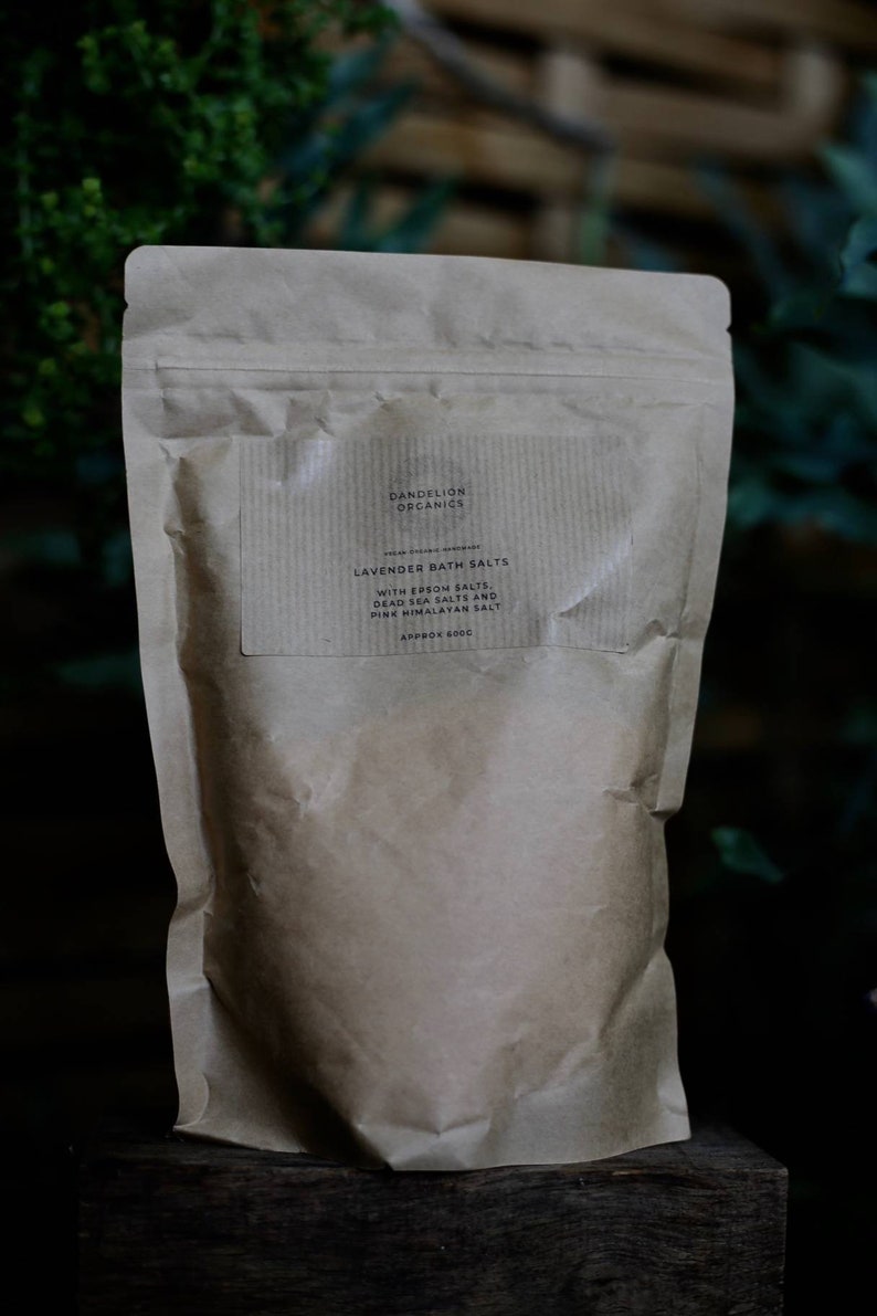 May include: A brown paper bag of Dandelion Organics Lavender Bath Salts. The label reads "With Epsom Salts, Dead Sea Salts and Pink Himalayan Salt." The bag is sealed and appears to contain approximately 600g of product.