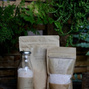 May include: A clear glass bottle and two brown paper pouches filled with bath salts. The bottle has a silver cap and a brown label that reads "Grapefruit Bath Salts". The pouches are labeled "Lavender Bath Salts" and "Orange Bath Salts".