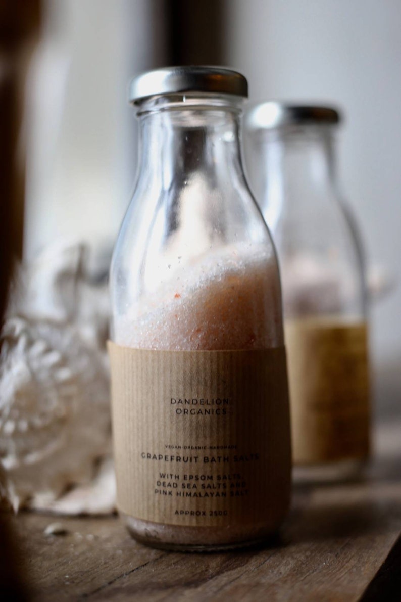 May include: Clear glass bottle filled with pink grapefruit bath salts, with a silver lid and a brown paper label. The label reads "Dandelion Organics" and "Grapefruit Bath Salts". The bottle contains approximately 250g of bath salts.