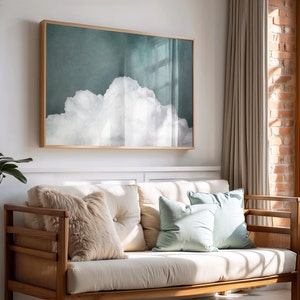 May include: A framed print of a white cloud against a teal background. The print is hanging on a white wall above a light brown sofa with light blue and cream cushions.