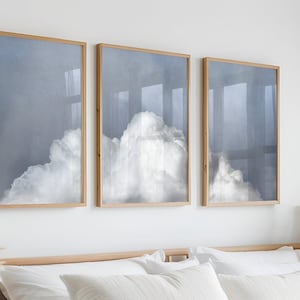 Könnte beinhalten: Drei gerahmte Drucke einer weißen Wolke vor blauem Himmel. Die Drucke sind in Holzrahmen gefasst und in einer Reihe an einer weißen Wand angeordnet.