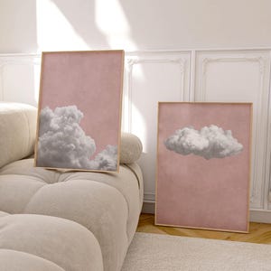 May include: Two framed prints with a pink background and white clouds. The print on the left has a large cloud in the bottom left corner. The print on the right has a single cloud in the center.